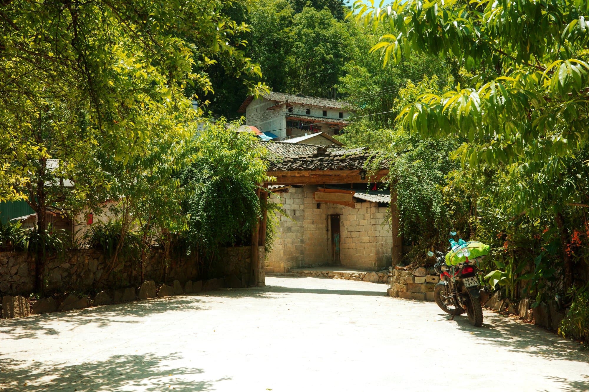 a motorbike standing on a small plastered area with an entry arch in the background
