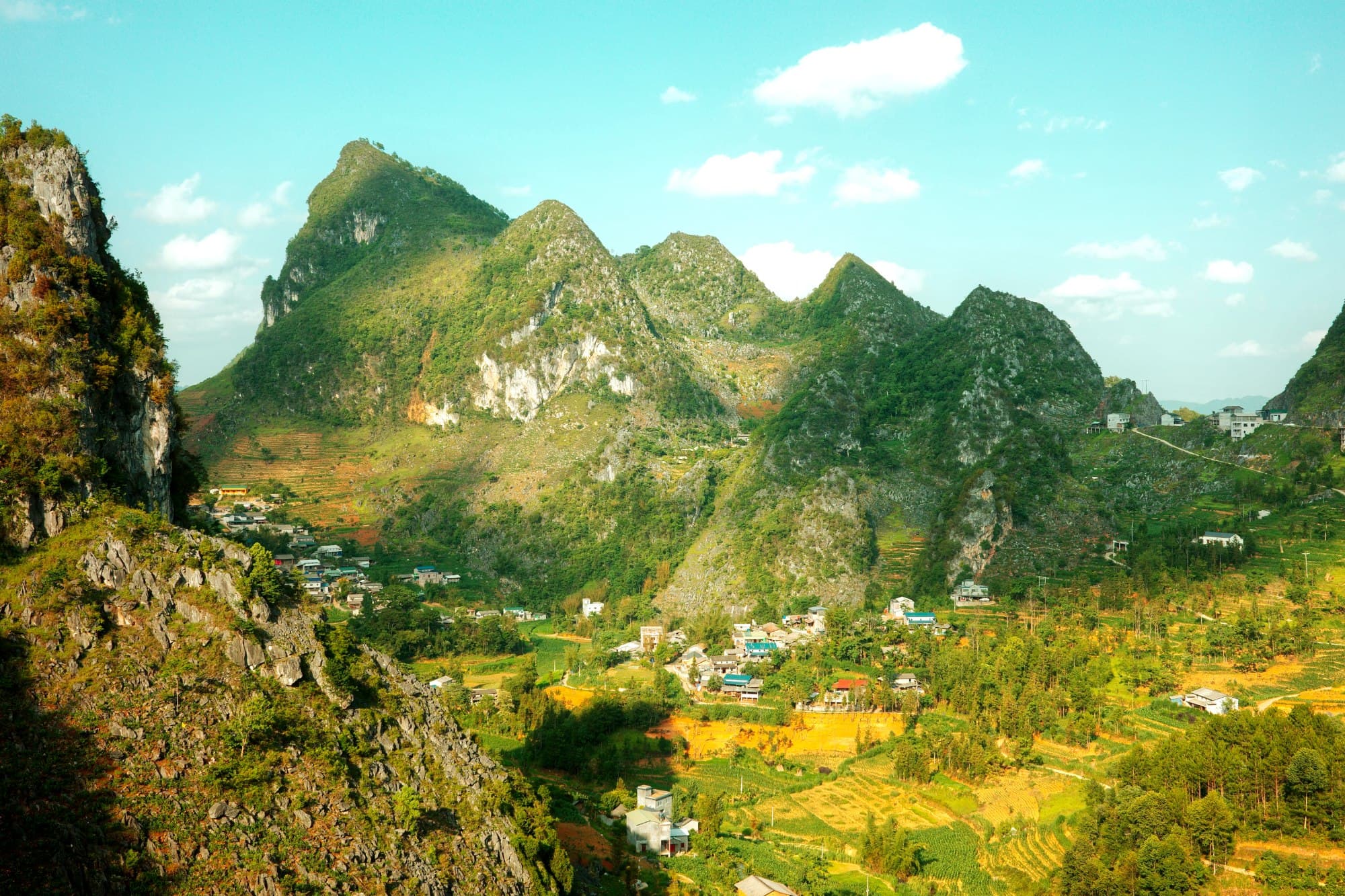 a large lush green mountain with a village at the foot of the mountain