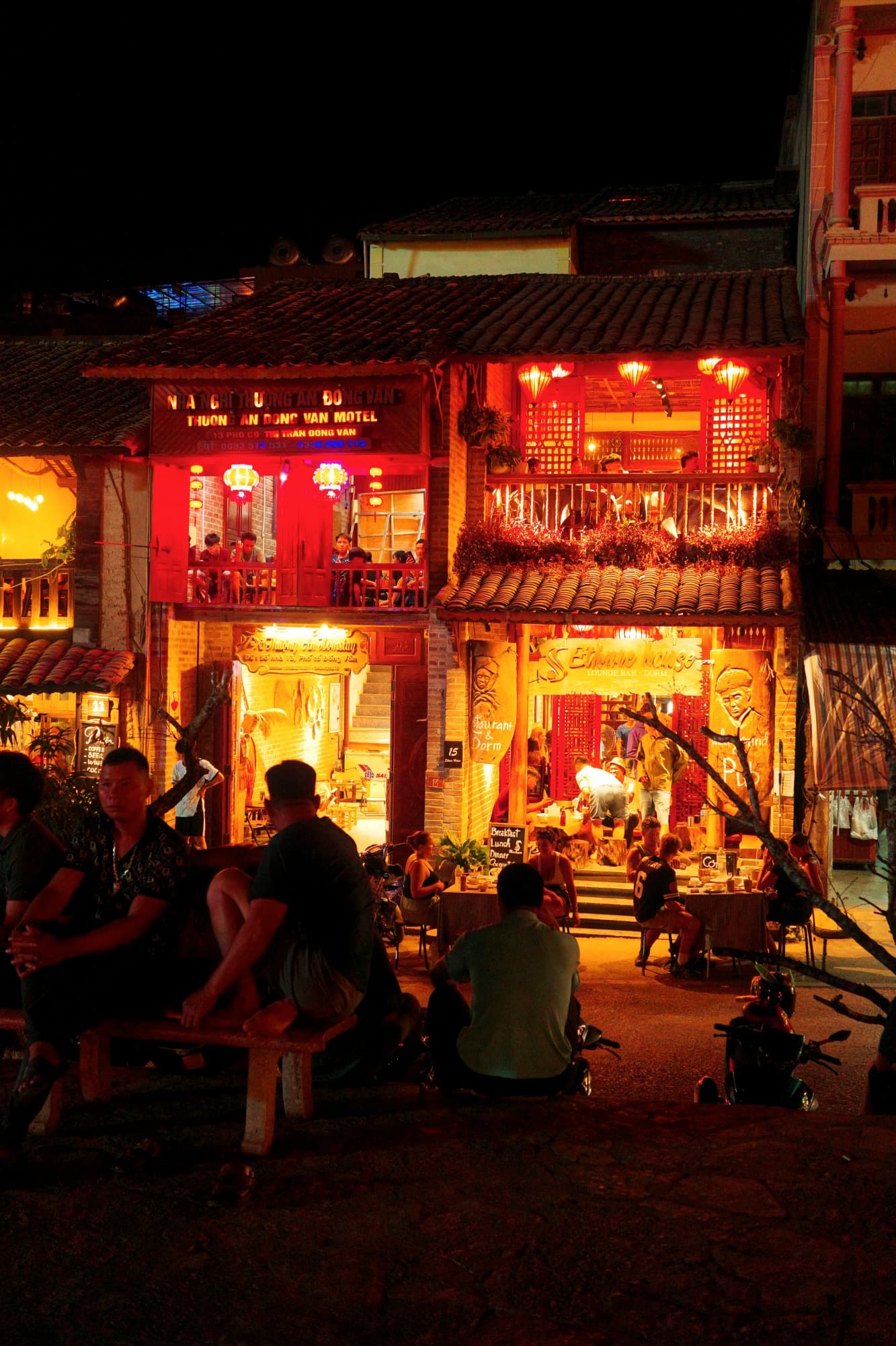 village life at night; people sitting on benches talking with some cozy open buildings in the background